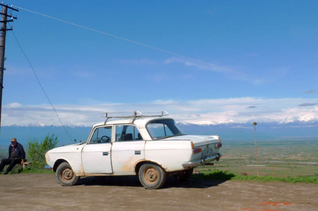 A classic car rests before the Alazani Valley and Caucasus peaks typical of Georgia's countryside.