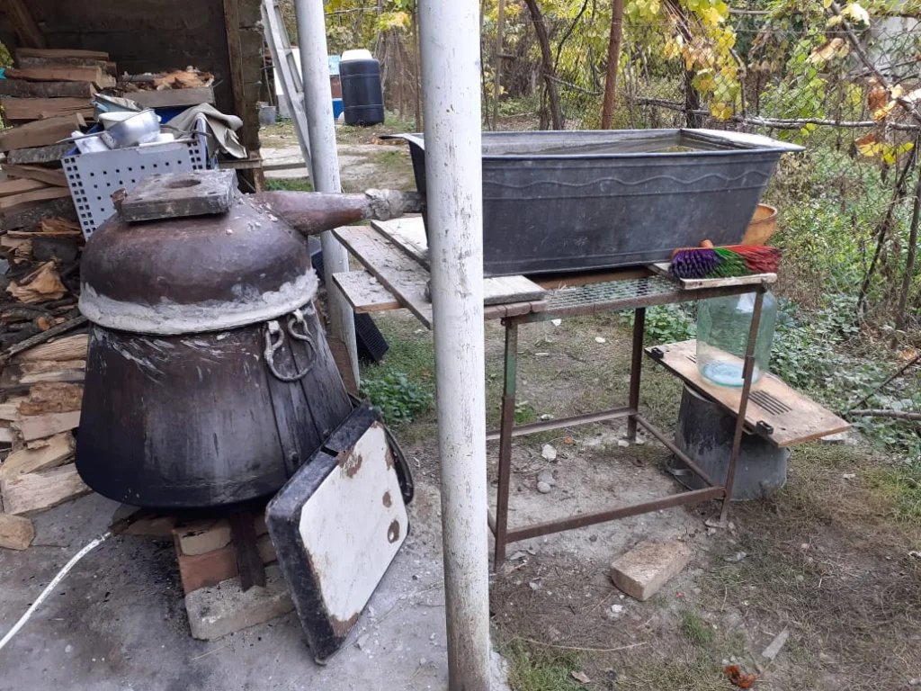A rustic copper pot still set up for home chacha distilling in a Georgian garden.