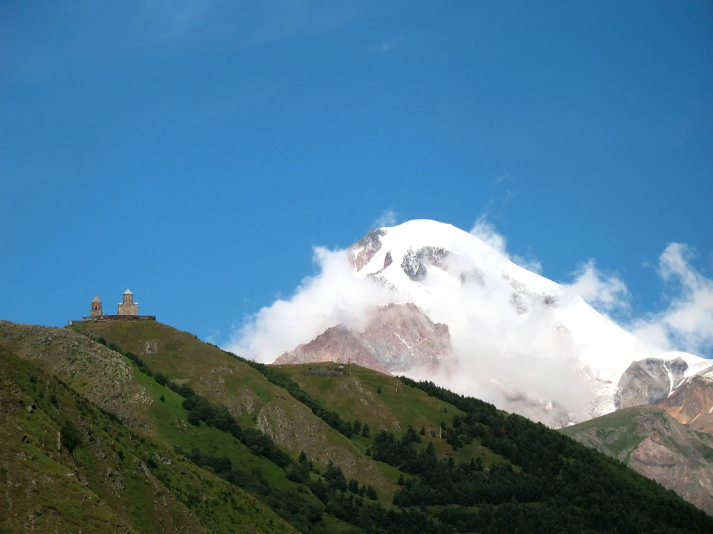 Gergeti Trinity Church perched on a green ridge beneath the snow-capped peak of Mount Kazbek.