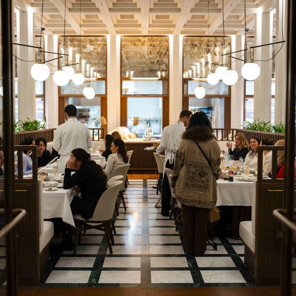 Grand Café — элегантный зал с мраморным полом, шарообразными подвесными светильниками и гостями за столами с белыми скатертями.