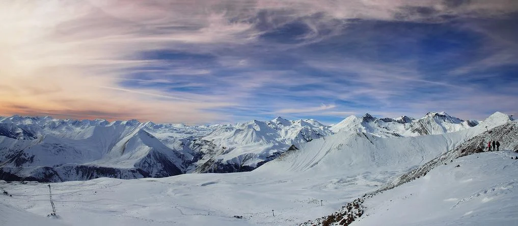 Panoramic snow-covered peaks surrounding Gudauri, the ski resort reached via this mountain road.