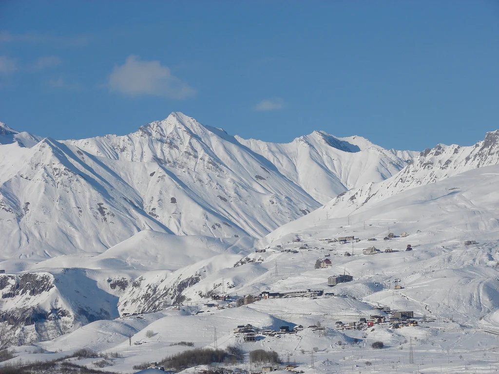 Snow-covered peaks and the scattered buildings of Gudauri ski village in the Greater Caucasus.