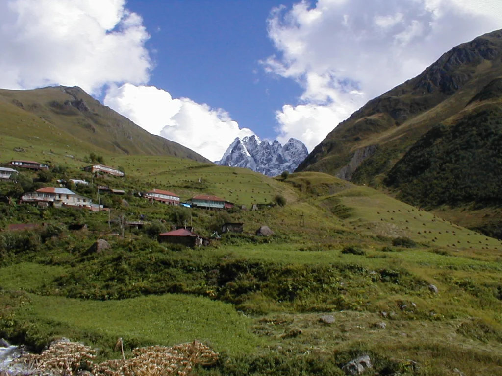 The village of Juta nestled in a green valley with the snow-capped Chaukhi massif beyond.