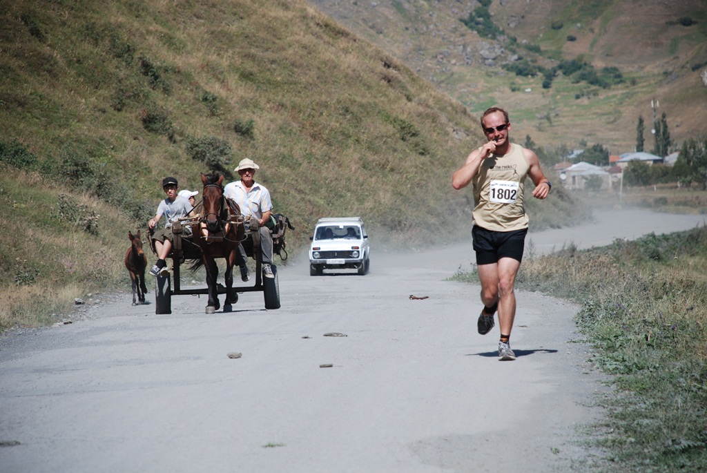 A competitor runs past a horse cart on the dusty trail of the Kazbegi Mountain Marathon.