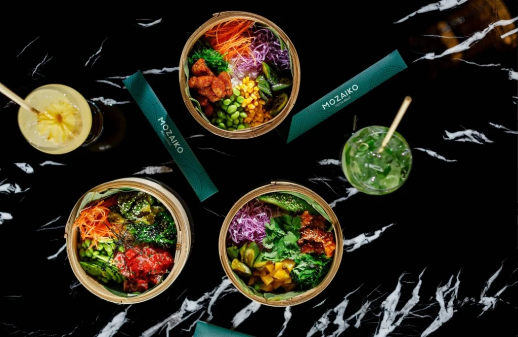 MOZAIKO — Overhead shot of colorful bamboo steamer bowls and drinks on a marble table at Mozaiko.