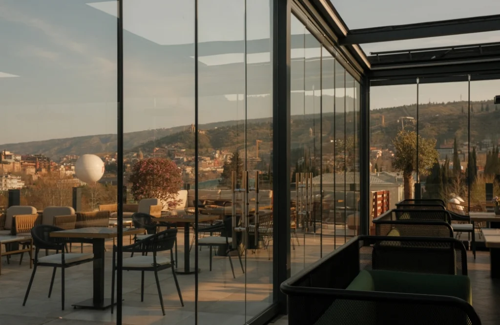 Mozaiko Terrace — Glass-enclosed rooftop terrace with seating overlooking the city skyline at sunset.