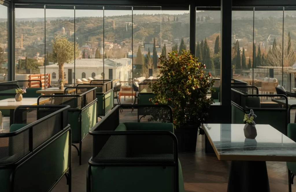 Mozaiko Terrace — Glass-enclosed terrace restaurant with green seating and city skyline backdrop.
