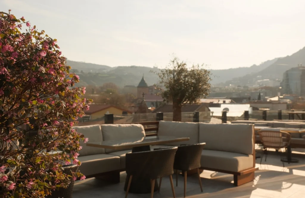 Mozaiko Terrace — Rooftop lounge seating with panoramic hillside and city view framed by flowering plants.