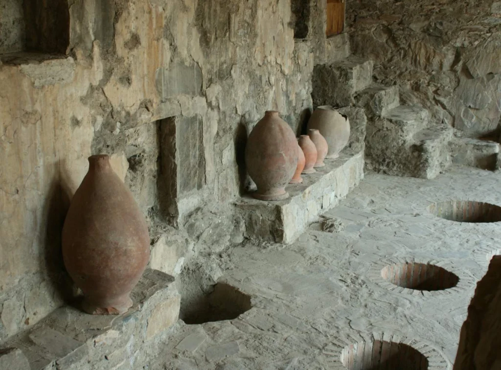 Qvevri wine jars lined along the stone walls of a historic Kakheti wine cellar.