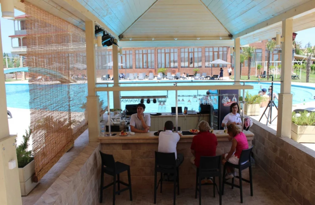 Pool Cafe — Guests seated at an outdoor poolside bar counter under a covered pavilion.