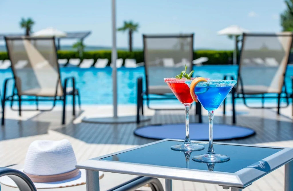 Pool Cafe — Two colorful cocktails on a poolside table with loungers in background.