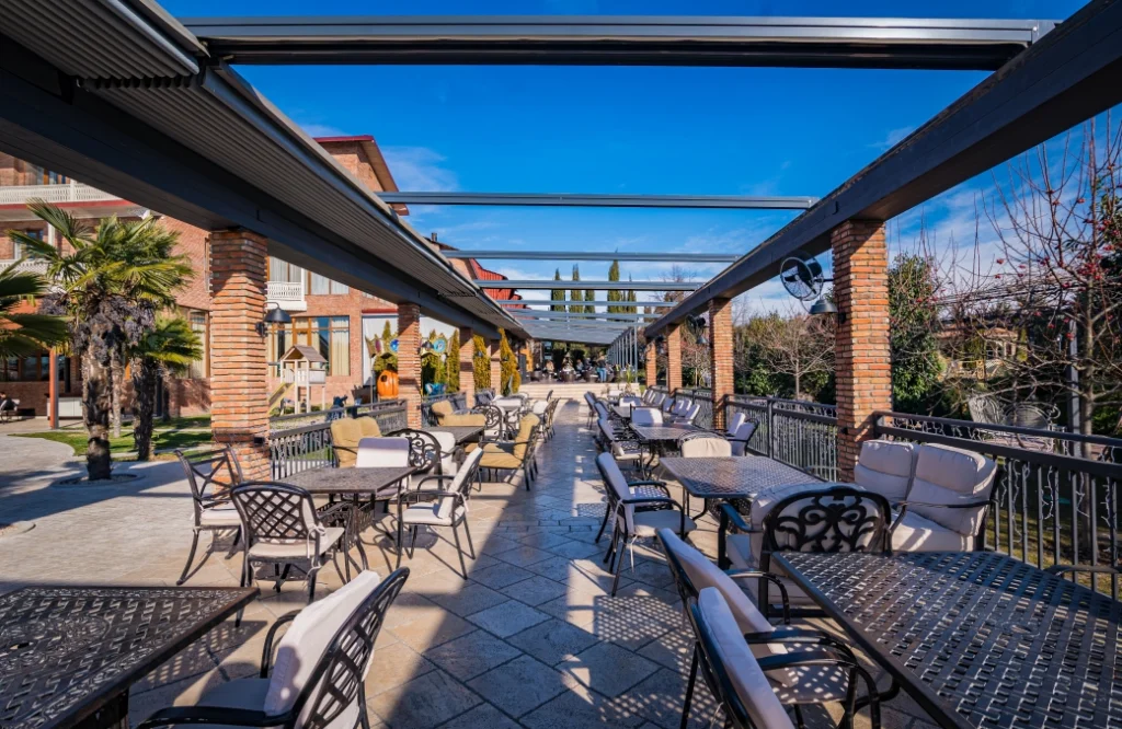 Restaurant & Lounge — Covered outdoor patio with dining tables under a pergola and daytime sky.