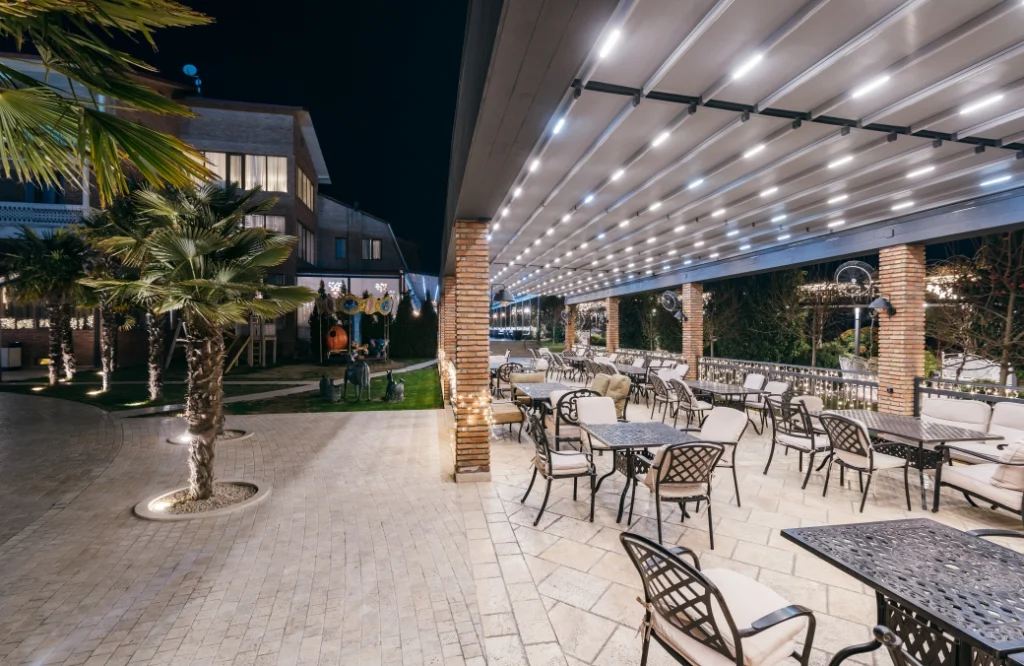 Restaurant & Lounge — Illuminated outdoor terrace at night with palm trees and view of the hotel facade.