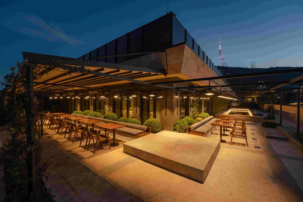 Rolling Stone Rooftop Bar — терраса на крыше с деревянными сиденьями и перголой, освещённая в сумерках.