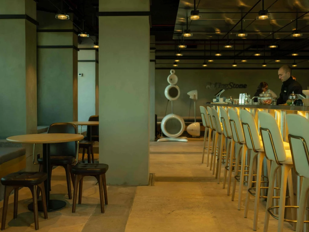Rolling Stone Rooftop Bar — зона бара со стульями, столами и декоративными подвесными скульптурами внутри помещения.
