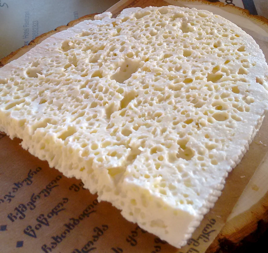 A sliced wheel of sulguni shows the characteristic layered, porous texture of Georgian cheese.