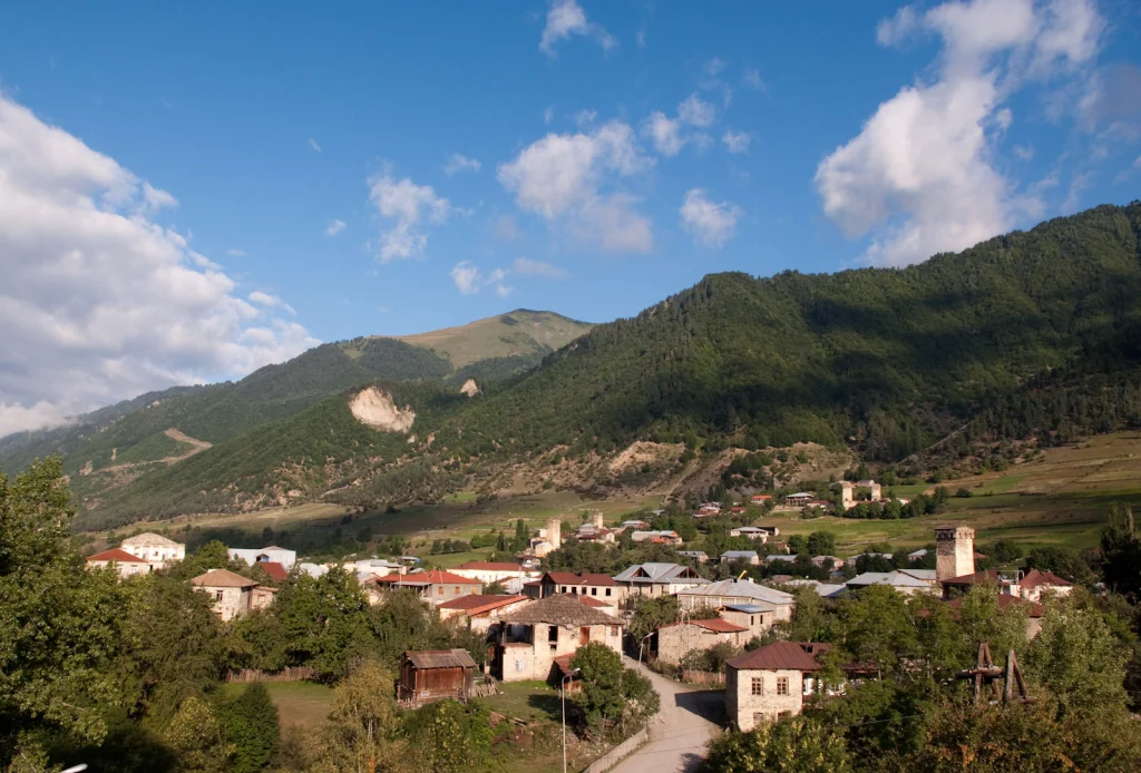 Mestia village with traditional Svan towers set against forested mountains and blue sky.