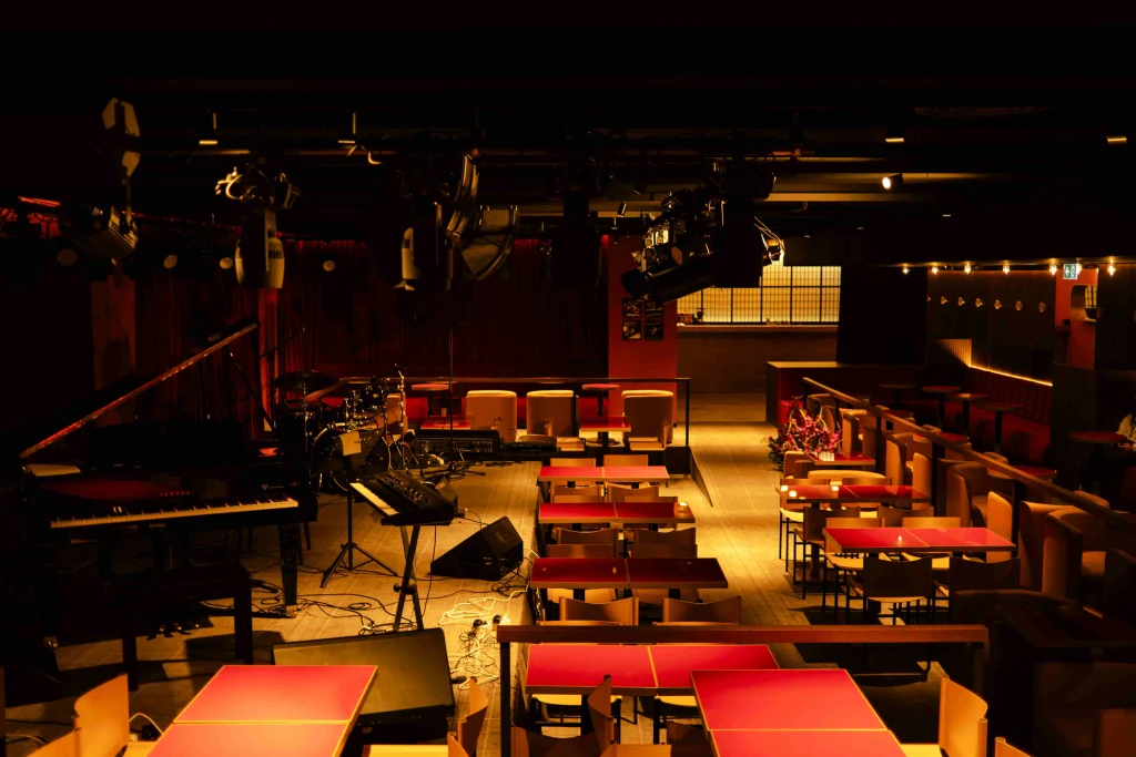 Tatuza Jazz Club — Overhead view of the jazz club's stage, piano, and red-topped tables under moody lighting.