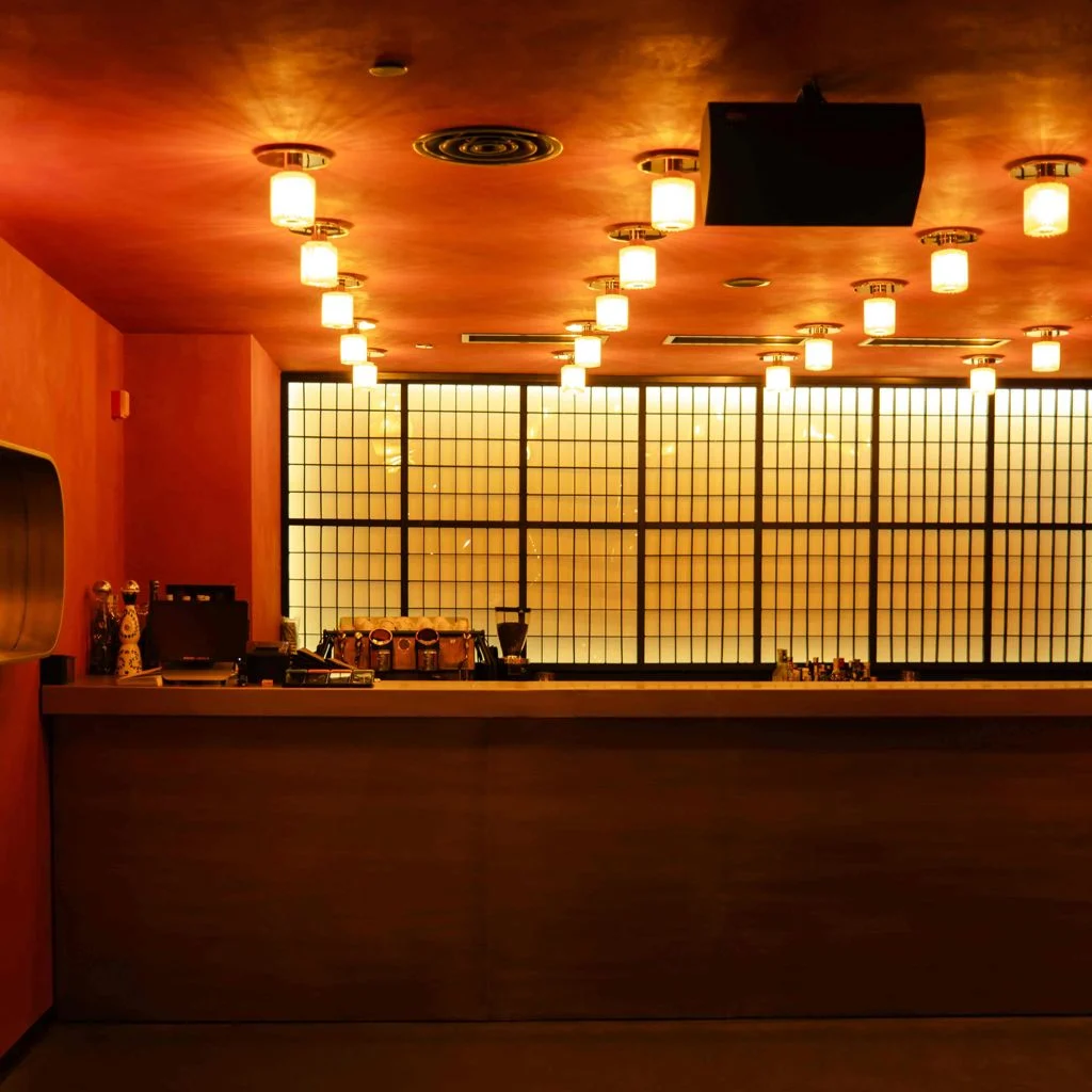 Tatuza Jazz Club — Illuminated bar counter with warm pendant lighting and a backlit screen panel.