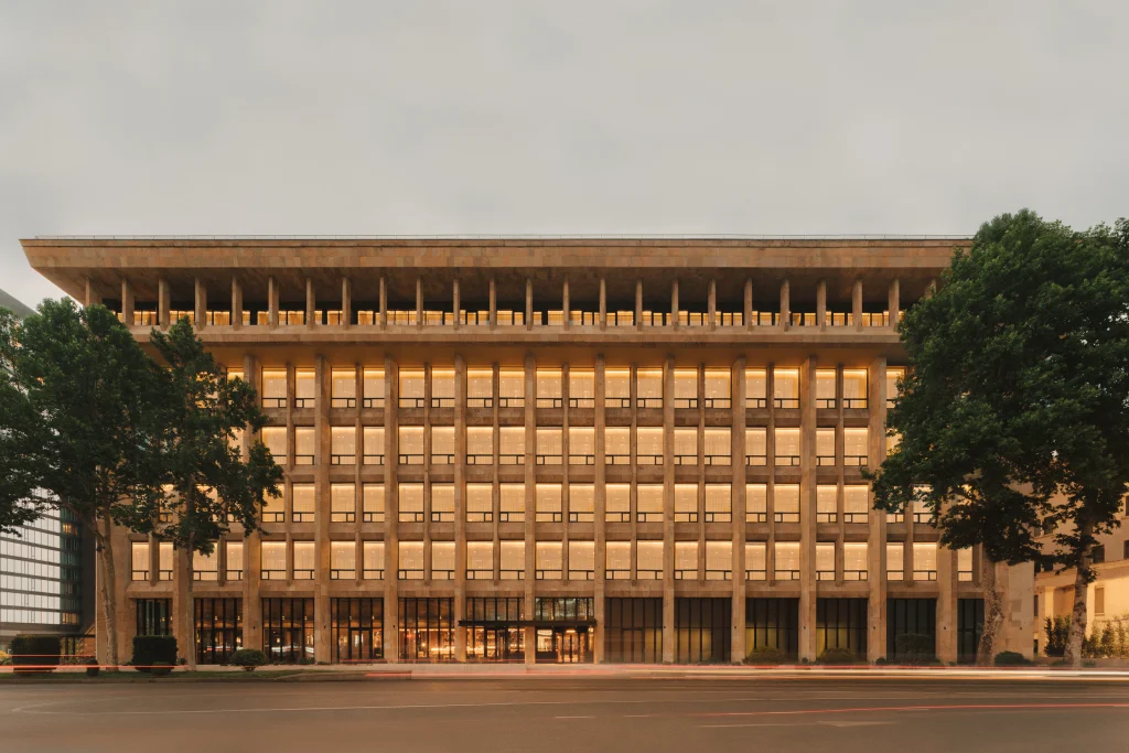 Telegraph Hotel — Columned stone facade of the hotel building illuminated at dusk with trees in front.
