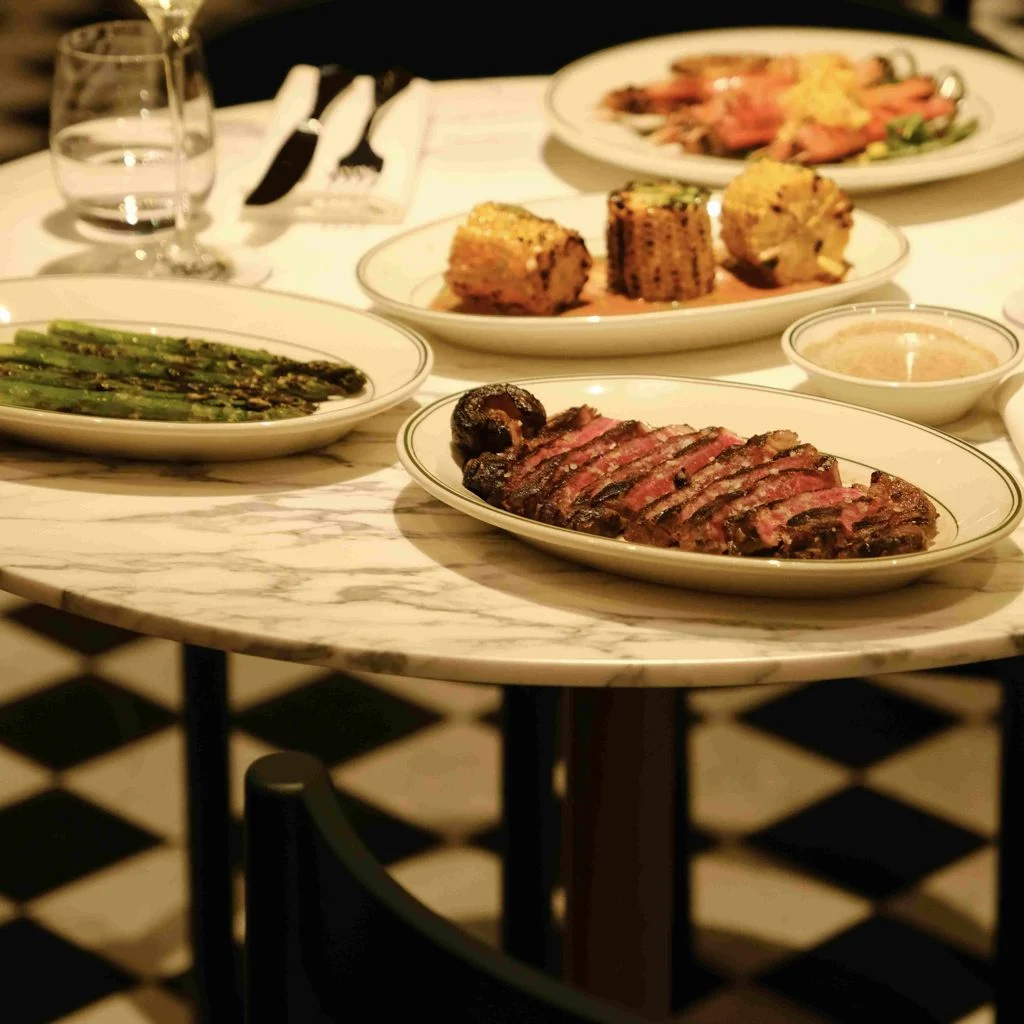 The Grill — Table spread of grilled steak, asparagus, corn, and seafood on a marble tabletop.