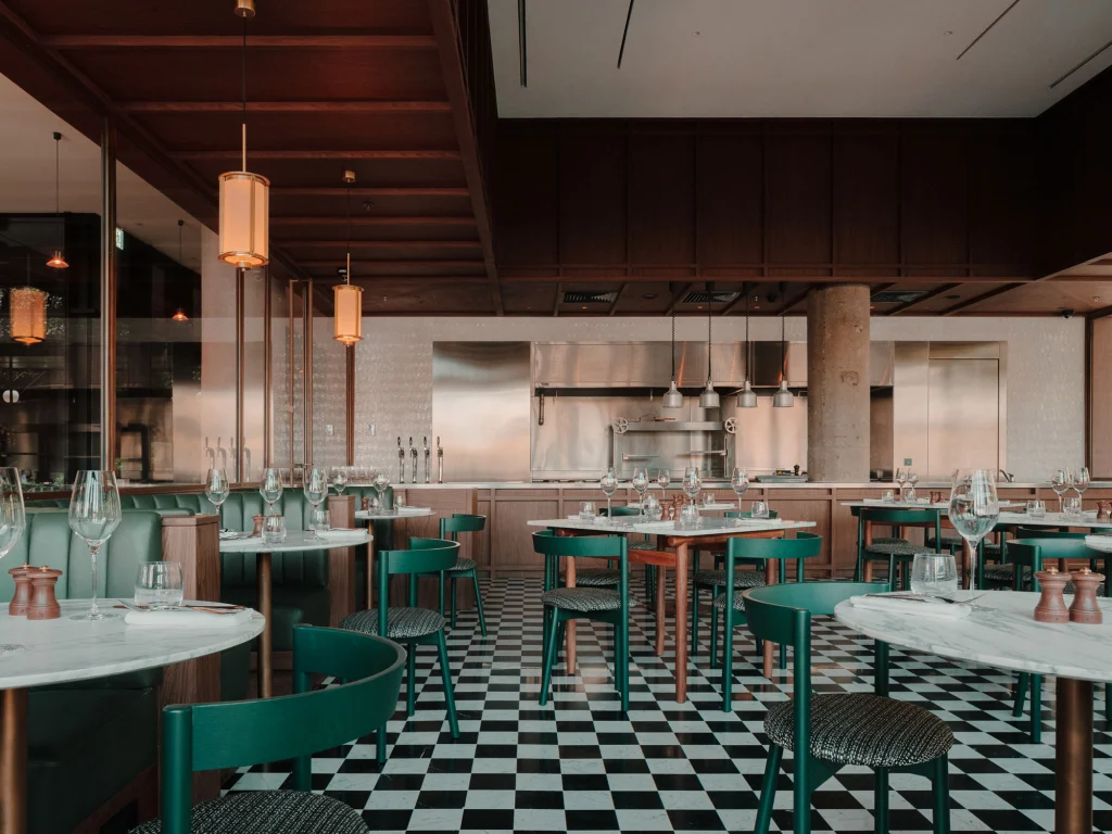 The Grill — Restaurant seating area with open kitchen pass, marble tables, and teal chairs.